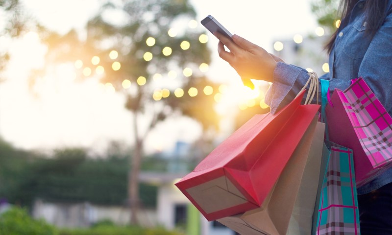 TIPS TO AVOID A HOLIDAY SPENDING HANGOVER | Woman holding phone and multiple holiday shopping bags