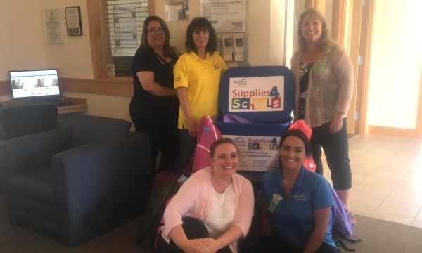 MID OREGON ANNOUNCES FUNDS MATCH | Mid Oregon Madras team celebrates 2019 school supply back pack donation around bin in branch.