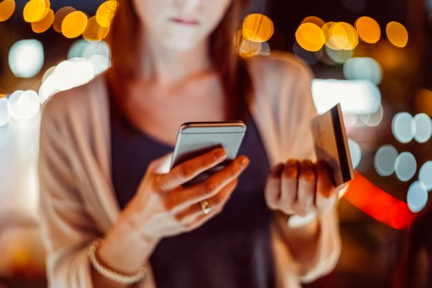 Woman holding phone and credit card wondering if her text is legit or a SMS scam